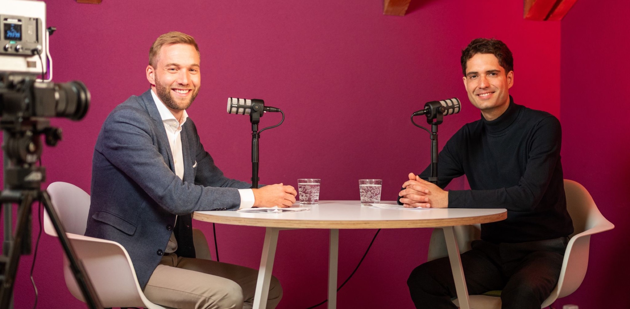 Zwei Gäste im Podcast-Gespräch vor magentafarbener Studiowand