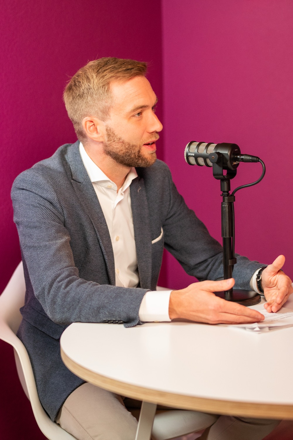 Gast im Gespräch am Podcast-Mikrofon vor magentafarbener Wand
